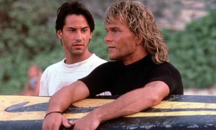 Keanu Reeves looking at Patrick Swayze who is holding a yellow and black surfboard