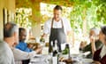 Sommelier pouring wine for men and women sitting at a restaurant's outside table