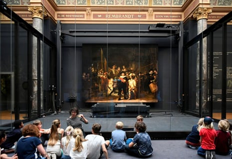 Children sitting on the floor listening to a teacher and looking Rembrandt’s large painting Night Watch at Rijksmuseum in Amsterdam