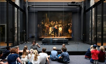 Children sitting on the floor listening to a teacher and looking Rembrandt’s large painting Night Watch at Rijksmuseum in Amsterdam