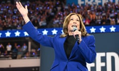 Kamala Harris in a blue suit, speaking into a mic gestures with one hand raised