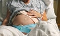 A pregnant woman sitting in a hospital bed holds a hand to her stomach