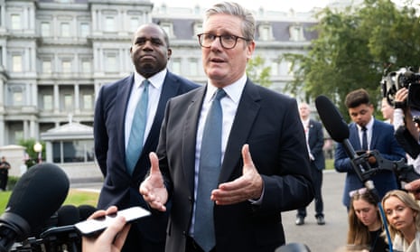 Keir Starmer with David Lammy standing behind him. Starmer is talking and they are surrounded by a crowd of journalists holding microphones and cameras.