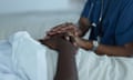 A nurse rests her hands on those of a patient lying in bed