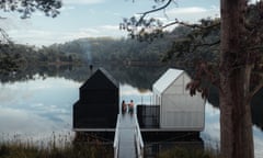 Two people sitting on a small jetty with two small structures on a still lake