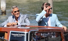 They stand on a boat in the sunshine, Clooney in grey jacket, Pitt in a pale blue one