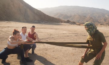 Three people pull on a fourth using a scarf around her waist, in the desert