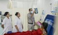 An Indian doctor stands by a patient in a bed holding up an X-ray while two female medics in white coats stand beside him