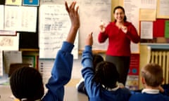 Children with their hands up in response to their teacher, in a lesson