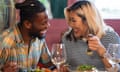 Close-up of restaurant setting, in which two models play people enjoying each others company over food and wine.