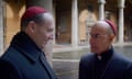 two men in dark coats with red cardinal's caps