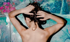 A close up of the bare back of a woman with her  hands clutching her hair