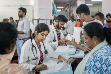 Young Indian doctors in a busy ward make notes in files while sitting opposite patients 