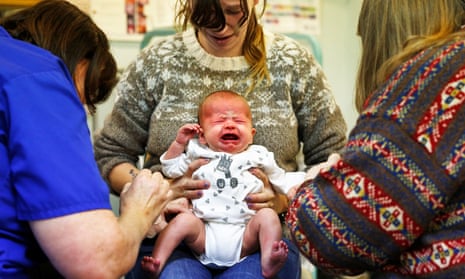 Crying baby receiving vaccination from health worker while being held by mother