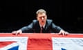 Thomas Coombes in a suit, leaning over a coffin draped in a union flag