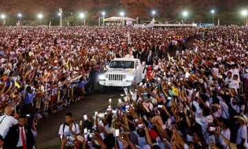 The pope stands in a car that is passing between crowds of people