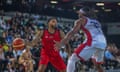 A basketball player tries to block another player in front of a large crowd