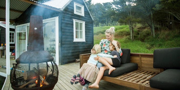 A woman sits on her porch next to a dark blue house, hugging her young son and daughter.