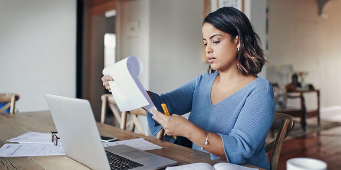 Woman in blue sweater looks over documents while sitting at her computer