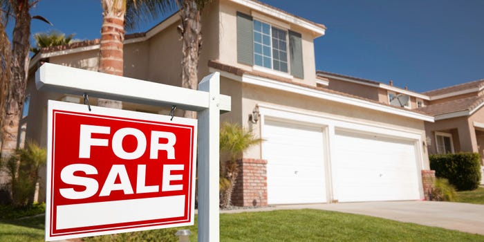 A red for sale sign sits in the front yard of a 2-story tan house