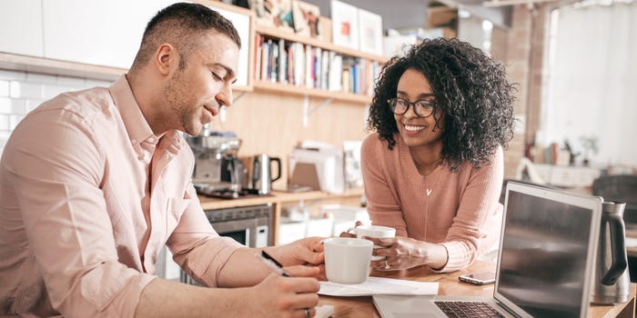 A photo of a young couple at a kitchen table working on finances.