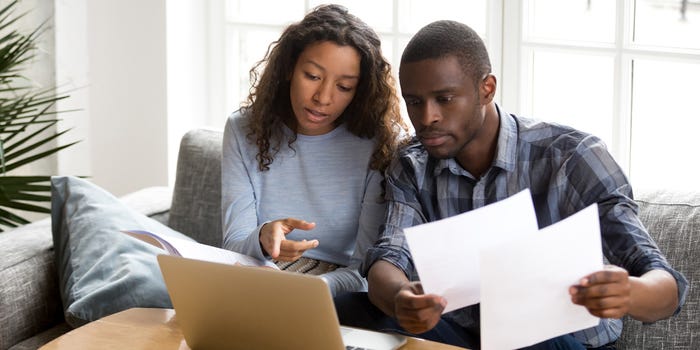 A photo of a young couple examining paperwork while working with a laptop computer at home.