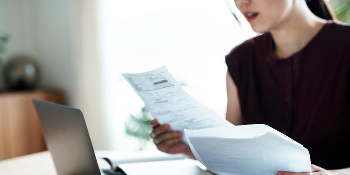 A photo of a person looking at financial documents in front of a laptop computer at home.