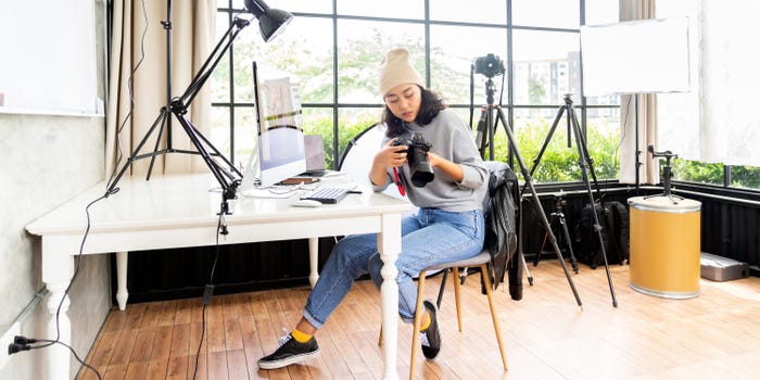 Woman sitting in a room with photography equipment looks at a camera