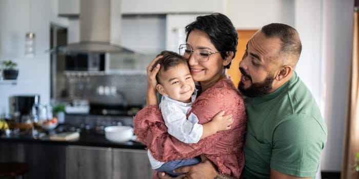 A man, woman, and young child embrace each other in a kitchen