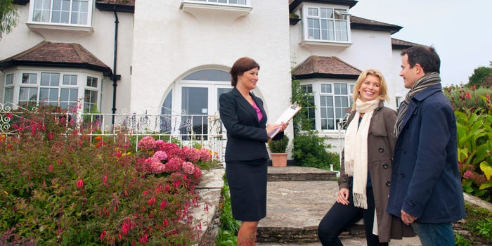 A man and a woman talk with their real estate agent in front of a home.