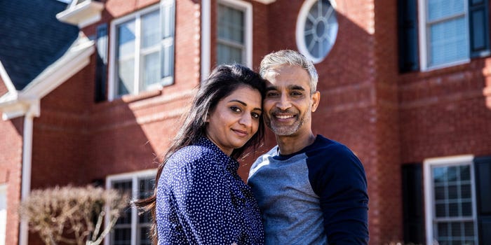 A man and woman stand in front of a large house