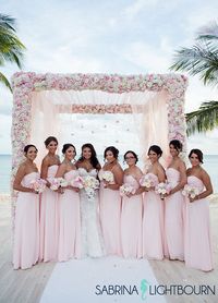 Bridesmaids gather around the bride wearing matching light pink gowns. #BeachWedding #PinkWedding