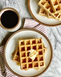 A rectangular waffle on a round plate, with a pat of butter, a cup of coffee, seen from above