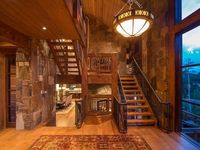 Warm foyer features stone walls and vaulted wood beam ceiling with a hanging pendant light. It has a wooden staircase that matches with the hardwood flooring.