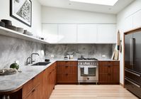 The finishes in the apartment were inspired by mid-century material palettes, with warm wood, creamy white walls, and earth tones. The couple have an extensive collection of souvenirs from traveling, so open display shelving was featured in the design. The custom kitchen cabinetry is walnut with a natural oil finish, which is a nice counterpoint to the warm Douglas-fir flooring. The stone countertops are a variety of marble called Fior Di Bosco, which has warm veins throughout.