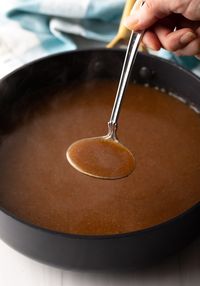 Metal ladle filled with gravy to camera.