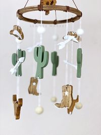 "This classic western baby crib mobile is one of my favorite designs to date. I love the vintage cowboy vibes and I'm sure you and your little rodeo baby will too! It has a cowboy riding a horse, two cowboy boots, two cowboy hats, two cattle skulls, four cacti, four accent arrows, four white wool pom balls and four tan wool pom balls. The wood tones paired with a neutral color palette and traditional brown (faux) leather make this piece both charming and rustic. The pieces are cut from pine, sta