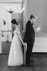 Black and white photo of bride and groom reading love letters back to back on wedding day. William Aiken House wedding. Bride and groom holding hands reading love letters. Wedding ideas. Wedding planning ideas. Wedding gown ideas. Wedding photography. www.kaileedimeglio.com Husband and wife photography team. destination luxury wedding photographer. kailee dimeglio photography