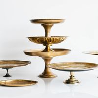 CAKE STANDS // BRASS A curated assortment of antique brass cake stands. These stands vary in shape, size, height, and tarnish. Color: Brass Rental Price: $25.00