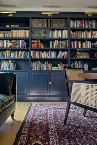 reading room, built in book shelves, painted blue book shelves, picture lights, seating for reading, reading nook, vintage rug, green velvet couch, cane chairs, cozy reading area, hardwood floors