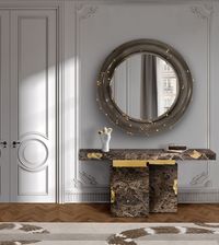 The Hallway itself is decorated in a traditional Parisian style, with intricate wall paneling and molding that adds texture and depth to the minimalist color palette of grays and whites. To the side, a decorative hand sculpture holds golden spheres, adding an artistic touch to the decor. The parquet wooden floor, along with the muted, abstract-patterned rug, complements the entire space with a warm, grounded feel. The overall ambiance is elegant, combining timeless Parisian architecture with modern, artistic decor elements.