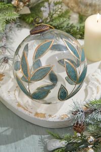 Discover the captivating beauty of our 6" Painted Laurel Glass Ornament. This masterpiece crafted from clear glass and elegantly outlined with gold accents is more than just an ornament; it's a work of art. The laurel leaf detail, traditionally associated with victory and honor, adds a touch of timeless sophistication. This ornament's luminous quality will transform your living space, casting a unique glow that captures the eye and the heart. This piece goes beautifully with other pieces in our