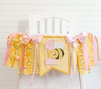 *Please check turn around times. All items are made to order* Our bumble bee high chair banner is super cute for any little one's birthday party! Fits standard high chair trays. Made with yellow and pink fabrics, poms, and completed with a #1 bee banner. All of our high chair tutus come with hook and loop fasteners attached so you can easily attach it to your high chair