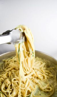 A serving of creamy vegan fettuccine being removed from the pot with a pair of tongs, with a white background.