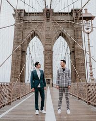 Waking up first thing in the morning for a pre-wedding shoot on the Brooklyn Bridge doesn't sound fun, but it's a lot better when your favorite person is with you.⁠ .⁠ [Two marriers, one in a blue suit and the other in a plaid suit, stand looking at each