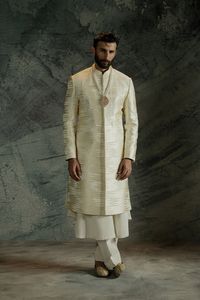 An ivory white closed sherwani detailed with a hidden placket and sloped band, adorned with textured chevron pattern embroidery in shades of gold and ivory white.

Fabric: Jamawar
Color: Ivory White