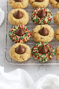 Our Gluten-Free Peanut Butter Blossoms recipe combines soft peanut butter cookies & chocolate kisses to make the perfect holiday cookie! They're a great recipe for a gluten-free Christmas cookie exchange or a great cookie for Santa. We use a simple trick to give this classic cookie the perfect soft texture. Don't miss all the cute ways to decorate these blossom cookies for the holidays! Get the recipe and more gluten-free holiday cookies to try at Sweets & Thank You