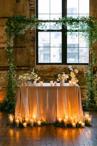 A wedding reception sweetheart table in front of the wedding arch with lots of candles