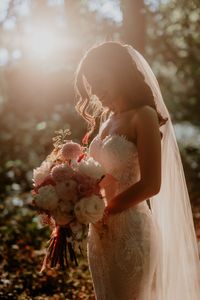 Bride stands in the sunshine as it begins to set during golden hour and golds bridal bouquet whilst wearing fitted Pronovias wedding dress | golden hour | bride style | colourful bouquet | lace wedding dress | golden hour portraits | The Kensington Photographer