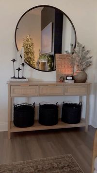 beautifully styled hallway. A large, round mirror creates a focal point, adding depth and brightness to the space. The table is adorned with elegant black candle holders, a rustic countdown sign, and a charming potted mini tree in a neutral vase. Underneath, black woven baskets provide both style and storage. This setup perfectly combines modern and rustic elements to create a warm and inviting entrance. #mirror #hallway #inspohome #home #interiordesignideas